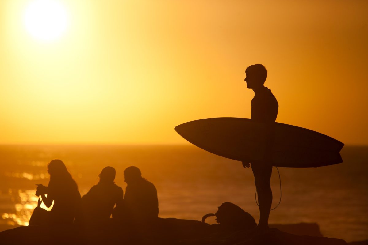 Surfer carrying surfboard on beach at sunset, Taghazout, Morocco